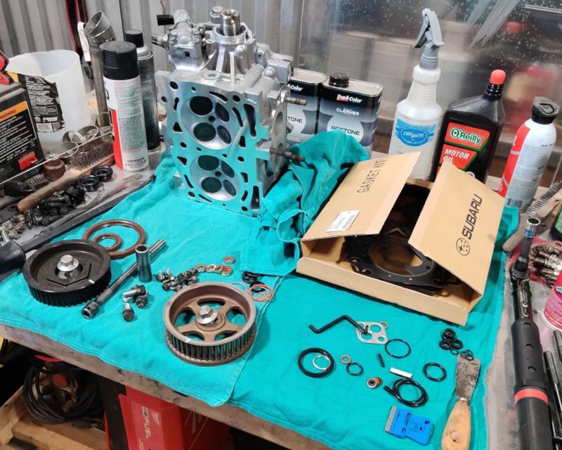 Subaru cylinder head and engine parts laid out on a workbench