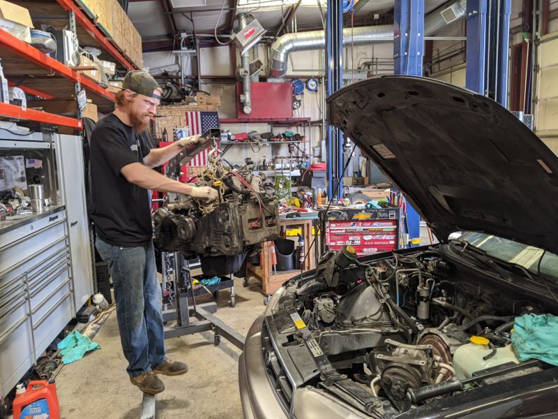 William pulling an engine on a hoist next to a car with its hood up